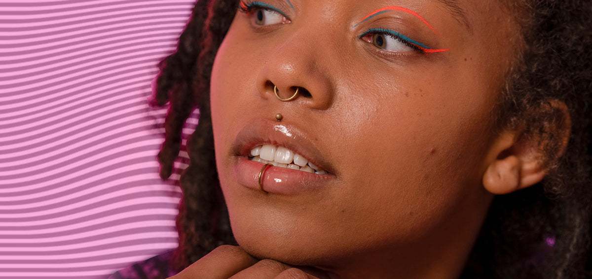 Woman with locs and colorful eyeliner wearing a gold-tone septum ring, a medusa stud and a lower lip ring